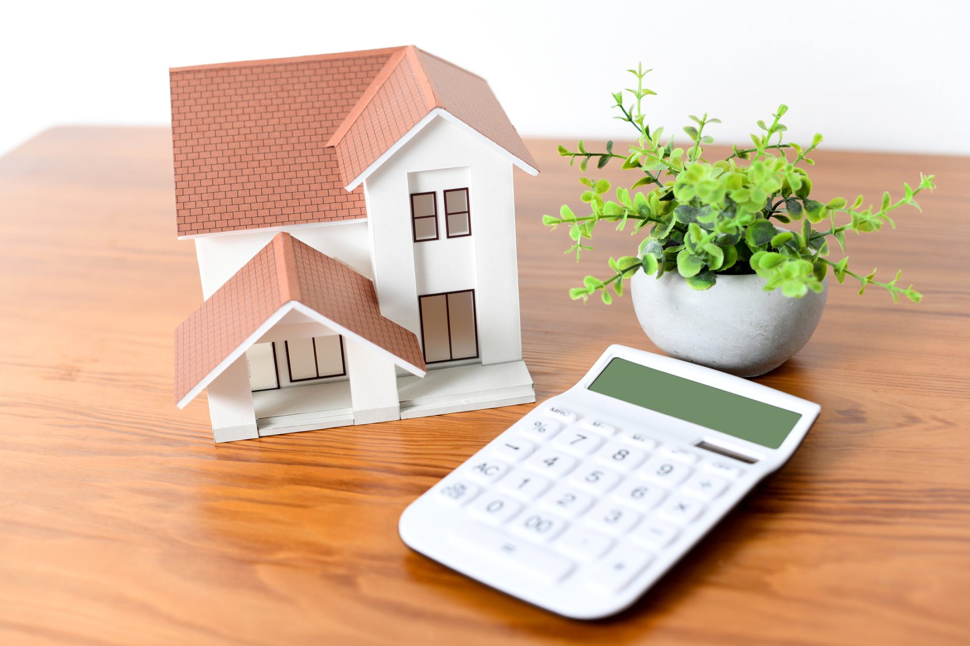 Modèle de maison miniature sur bureau à côté d'une calculatrice